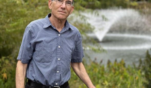 A man stands in front of an outdoor fountain. 